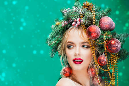 Portrait of a beautiful young woman with christmas tree in hairstyle decorated with beads and balls over blue background. Holiday make-up. Beauty, fashion.の写真素材