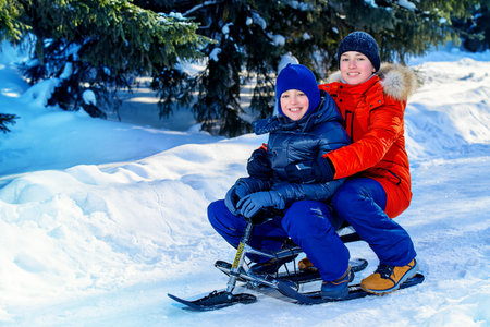Two happy boys sledding from a hill on a sunny winter day. Snow. Winter clothes. Winter activity.