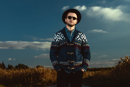 Autumn fashion. Portrait of a handsome man wearing cardigan and hat standing outdoor over autumn...
