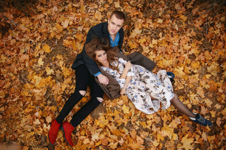 Autumn fashion. Beautiful fashionable couple lying on yellowed autumn grass and leaves.