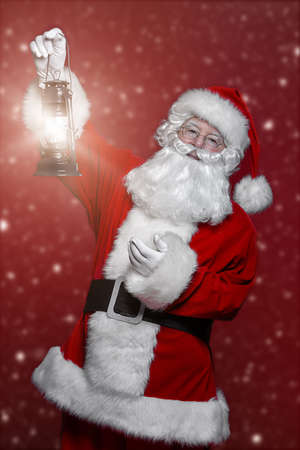 Christmas concept. Portrait of a fairytale Santa Claus holding lantern over red background. Magic time. Copy space. の写真素材