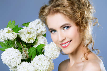 Summer, spring inspiration. Smiling young woman with natural make-up and beautiful curly hair posing with white flowers. Beauty, fashion, cosmetics. の写真素材