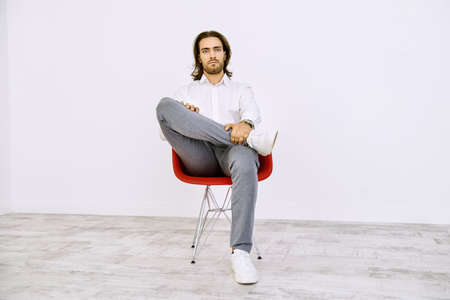 Handsome young man on a red armchair in a white room. Male beauty, fashion. Interior and furniture.の写真素材