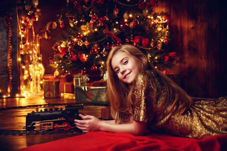Cute girl playing with a toy railway near the Christmas tree. Christmas night. Christmas decoration.の写真素材