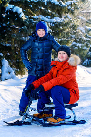 Two happy boys sledding from a hill on a sunny winter day. Snow. Winter clothes. Winter activity.の写真素材