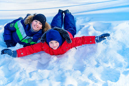 Two happy boys sledding from a hill on a sunny winter day. Snow. Winter clothes. Winter activity.の写真素材