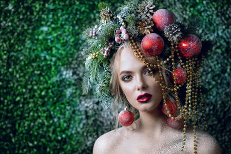 Close-up portrait of a beautiful young woman with christmas tree in hairstyle and holiday make-up over snow-covered green background. Beauty, fashion.の写真素材