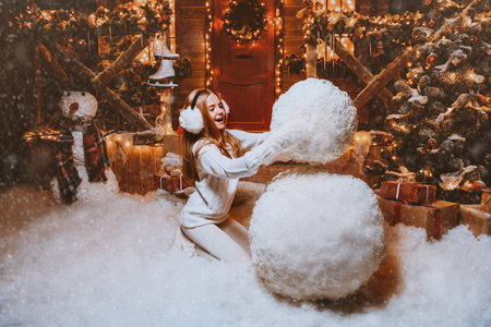 Pretty child girl sculpts a snowman near her house decorated for Christmas. Merry Christmas and...