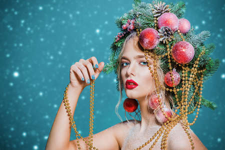 Portrait of a beautiful young woman with christmas tree in hairstyle decorated with beads and balls over blue background. Holiday make-up. Beauty, fashion.の写真素材