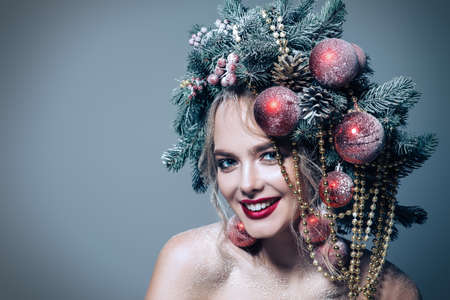 Portrait of a beautiful young woman with christmas tree in hairstyle decorated with beads and balls. Holiday make-up. Beauty, fashion.の写真素材