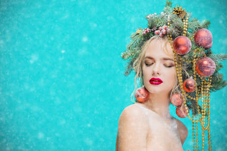 Portrait of a beautiful young woman with christmas tree in hairstyle decorated with beads and balls over blue background. Holiday make-up. Beauty, fashion.の写真素材
