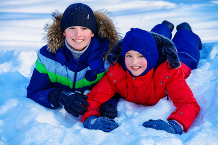 Two happy boys playing together outdoor on a sunny winter day. Snowfall. Winter clothes. Winter activity.の写真素材