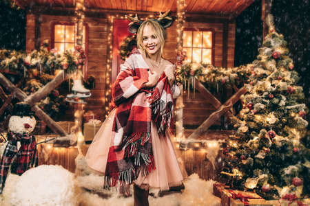 Happy girl in a beautiful dress, wrapped in a blanket, stands near the house decorated for Christmas. Time for miracles. Merry Christmas and Happy New Year.の写真素材