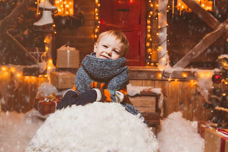 Cute child boy made a big snowball for a snowman near his house decorated for Christmas. Merry Christmas and Happy New Year.の写真素材
