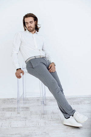 Full length portrait of a handsome young man on a chair. Male beauty, fashion. Furniture, interior concept. の写真素材