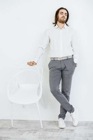 Full length portrait of a handsome young man on a chair. Male beauty, fashion. Furniture, interior concept. の写真素材