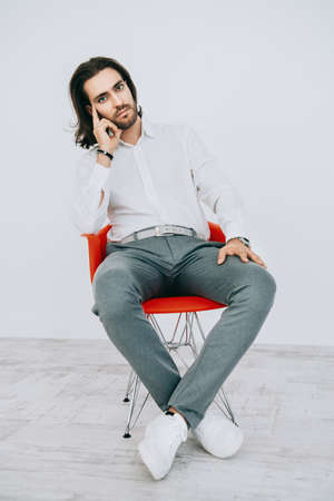 Handsome young man on a red armchair in a white room. Male beauty, fashion. Interior and furniture.の写真素材