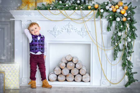 Cute three-year-old boy in elegant evening clothes poses in a beautiful room near fireplace decorated for Christmas. Luxurious apartments decorated for Christmas. Merry Christmas and Happy New Year.の写真素材