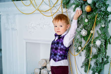 Cute three-year-old boy in elegant evening clothes poses in a beautiful room near fireplace decorated for Christmas. Luxurious apartments decorated for Christmas. Merry Christmas and Happy New Year.の写真素材