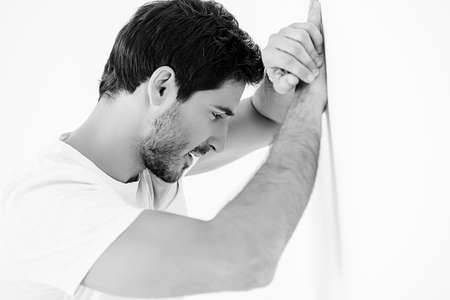 Handsome young man leaned against the white wall. Men's beauty and health.の写真素材