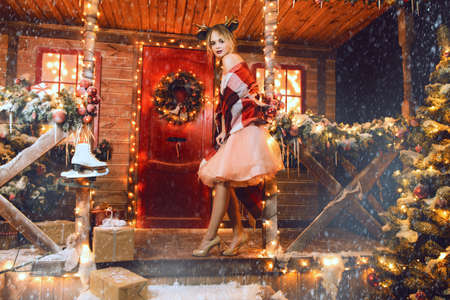 Happy girl in a beautiful dress, wrapped in a blanket, stands near the house decorated for Christmas. Time for miracles. Merry Christmas and Happy New Year.の写真素材