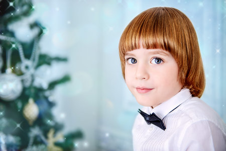 Cute five-year-old boy poses near the Christmas tree. Classic luxurious interior decorated for...