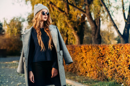 Seasonal autumn fashion. Modern young woman wearing fashionable warm clothes posing in the autumn park.の写真素材