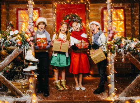 Four happy children stand with gifts near the house decorated for Christmas. Merry Christmas and Happy New Year. Winter holidays concept.の写真素材