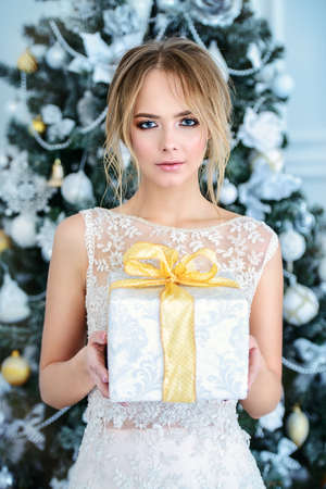 Beautiful young woman in evening dress, hairstyle and make-up holding a gift box. Luxurious apartments decorated for Christmas. Beauty, fashion.の写真素材