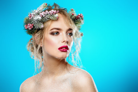 Portrait of a beautiful young woman with christmas tree in hairstyle and holiday make-up over blue...