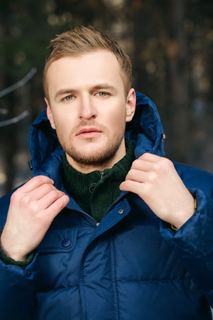 Portrait of a young man in a jacket with a hood. Man stands in winter forest.