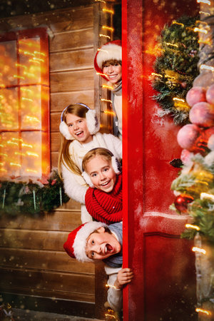 Group of children peeks out from behind the door of the house decorated for Christmas. Merry Christmas and Happy New Year.の写真素材