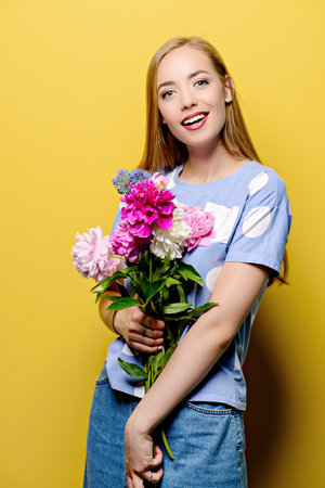 Portrait of a beautiful smiling young woman with a bouquet of summer flowers over bright yellow...
