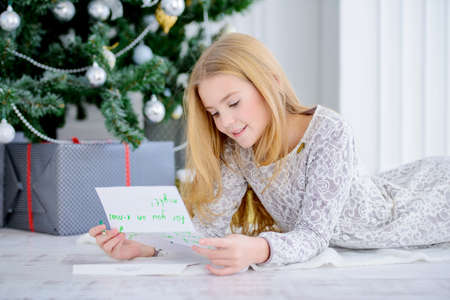 Cute girl near the Christmas tree writing a letter to Santa Claus. Christmas concept. Belief in miracles.の写真素材