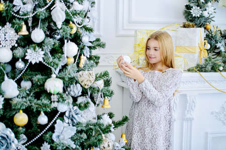 Happy child girl in a beautiful white dress decorates the Christmas tree. Merry Christmas and Happy New Year.の写真素材