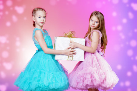Two pretty little girls dressed in beautiful festive dresses  with gift boxes in their hands. Kid's...