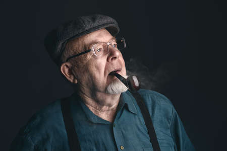 Portrait of a smiling old man smoking a pipe. Black background. Old age concept.の写真素材