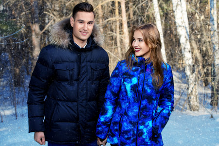 Couple of young people in winter clothes in the park. Winter fashion. Down jacket.