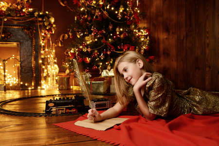 Cute girl near the Christmas tree writing a letter to Santa Claus. Christmas concept. Belief in miracles.の写真素材