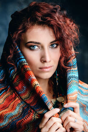 Close-up portrait of a beautiful red-haired woman wears a kerchief and earrings in boho style. Ethnic style in accessories.の写真素材