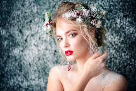 Close-up portrait of a beautiful young woman with christmas tree in hairstyle and holiday make-up over snow-covered green background. Beauty, fashion.の写真素材