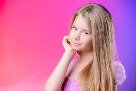 Portrait of a cute nine year old girl in an elegant dress over pink background. Children's beauty and health. の写真素材