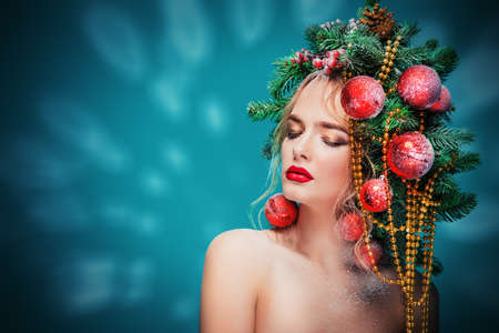 Portrait of a beautiful young woman with christmas tree in hairstyle decorated with beads and balls over blue background. Holiday make-up. Beauty, fashion.の写真素材
