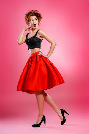 Beautiful emotional young woman wearing skirt and top blouse poses over pink background. Pin-up style. Fashion studio shot. Full length portrait. の写真素材
