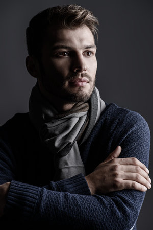 Handsome young man in scarf and sweater. Studio portrait. Autumn and winter clothing. Male fashion.