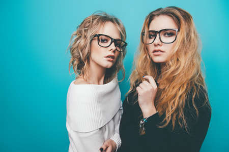Two pretty girls in glasses are posing in studio over blue background. Beauty, fashion. Optics, eyewear.の写真素材