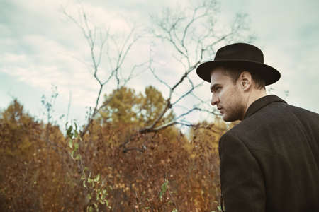 Seasonal autumn fashion. Portrait of a handsome man wearing black coat, and a hat.  Autumn nature.の写真素材