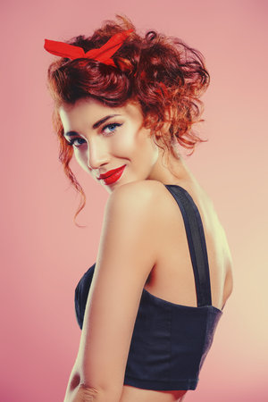 Portrait of a funny emotional young woman with curly foxy hair and a red bow on hair. Pin-up style....