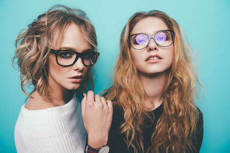 Two pretty girls in glasses are posing in studio over blue background. Beauty, fashion. Optics, eyewear.の写真素材