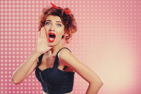 Pretty emotional girl with curly foxy hair shouts, putting his hand to his mouth. Pin-up style.の写真素材